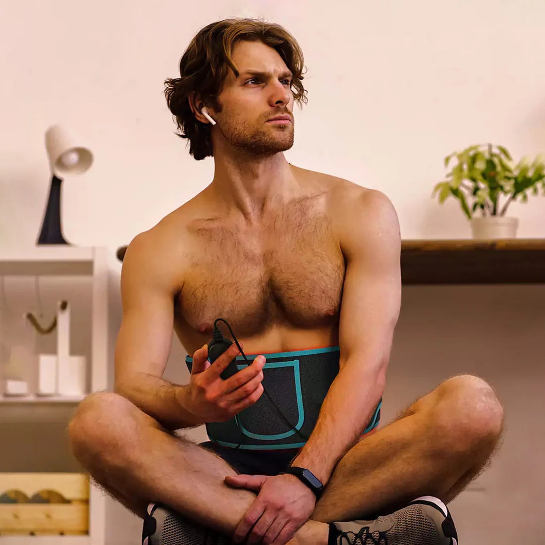 Férfi edzés utáni pihenés közben fényterápiás övet visel; regeneráció, izomlazítás és zsírégetés elősegítésére.