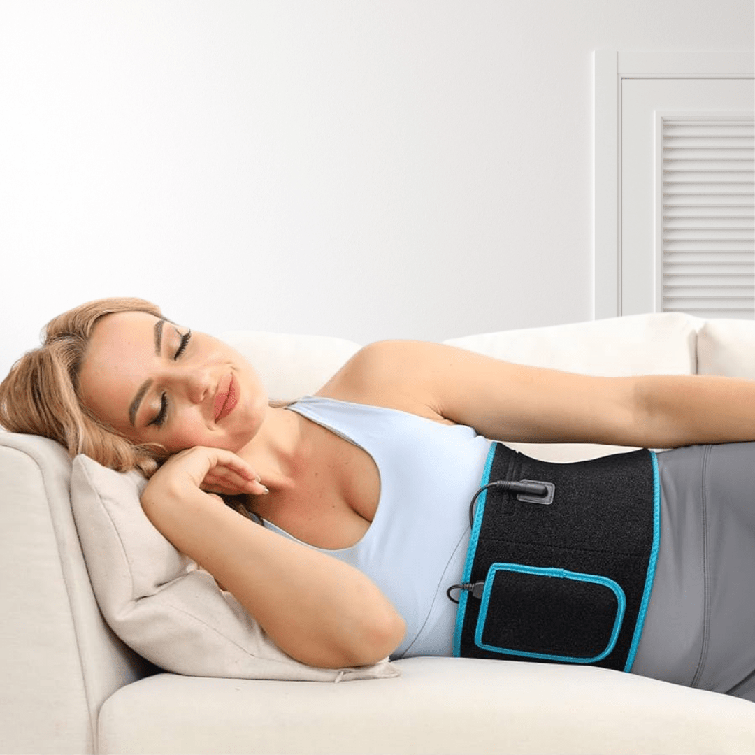 Nő kanapén pihen, hasán vörös fényterápiás szalaggal; zsírbontás és bőrtónus javításnak támogatása.